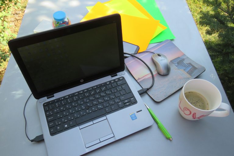 laptop and cup of tea with notes on a table outside in the sun